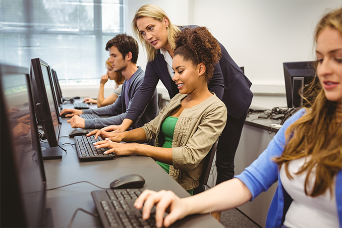 Trainerin erklärt Teilnehmer*innen etwas am Computer